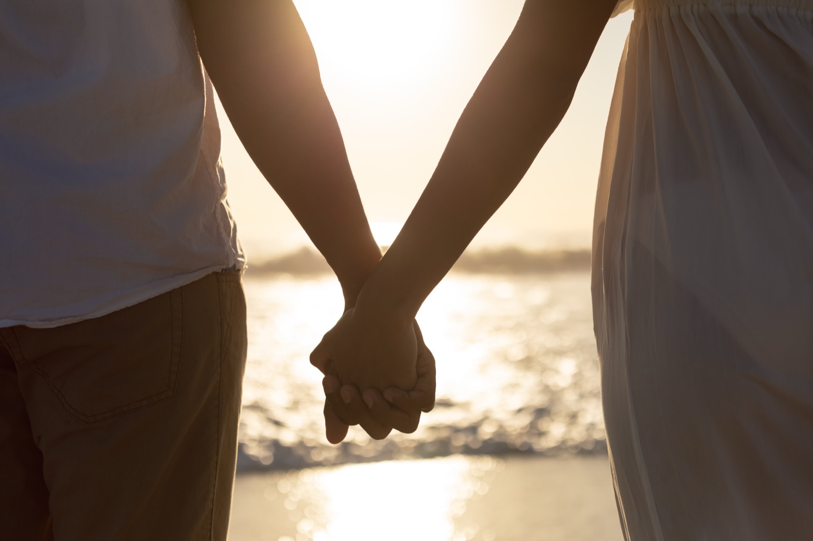 A couple holding hands on the beach at sunset