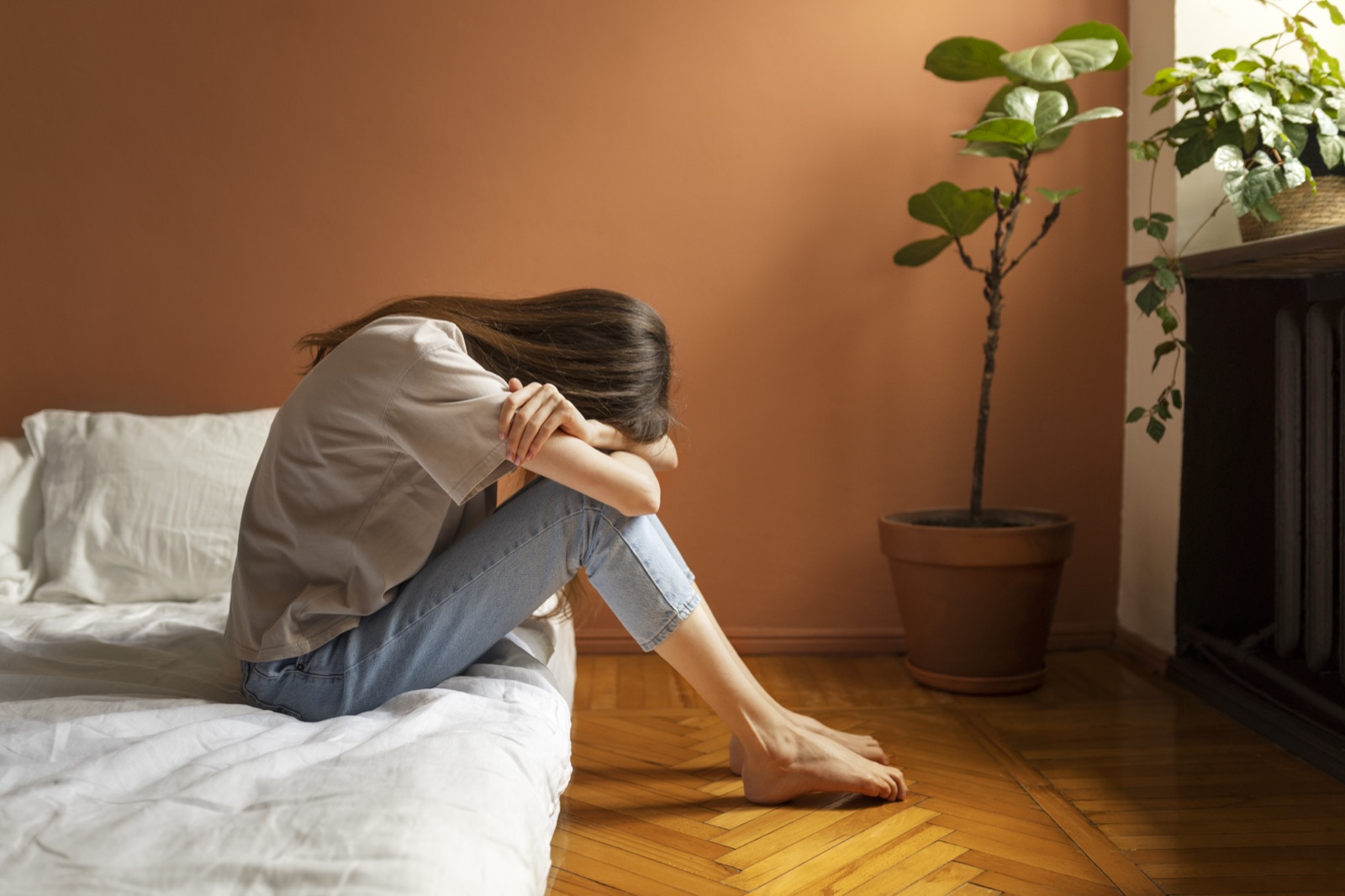 A woman sitting on the edge of a bed with her head resting on her knees
