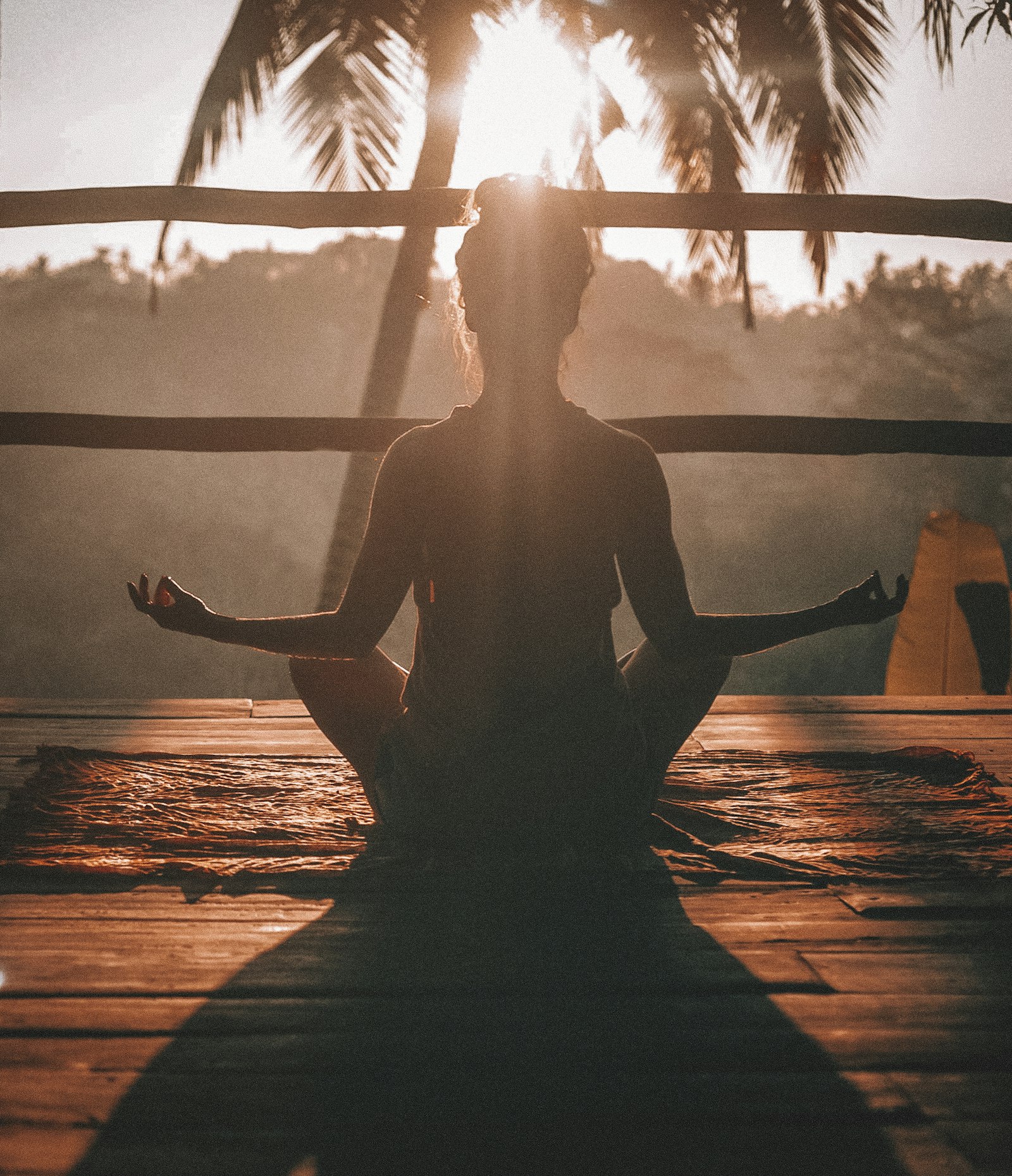A person meditating peacefully at sunrise, framed by palm trees
