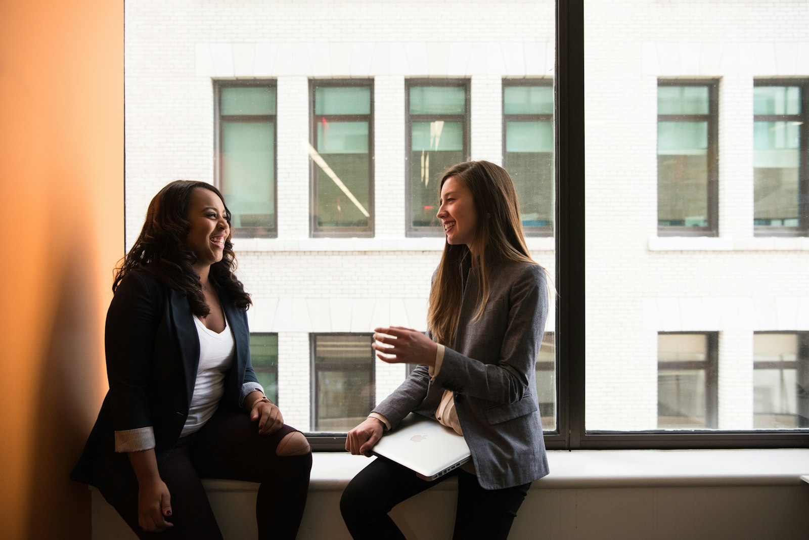 Two women sitting by a window, talking warmly and laughing together